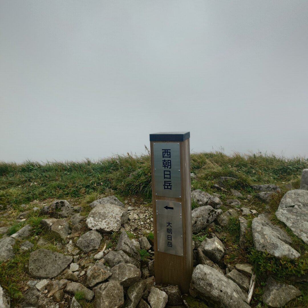 霧に包まれた西朝日岳の山頂標